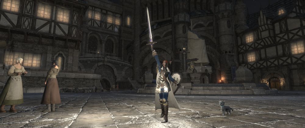 A brown-skinned female Miqo'te from FFXIV. She's holding a cruciform hilt sword in her right hand up high, with a shield held behind her on her left arm. Her armor is a segmented breastplate and tassets, with a wide leather sash from her right shoulder down to her left hip. Her arming coat and pants are a deep, almost navy blue. She has a white cloak draped over her shoulders.