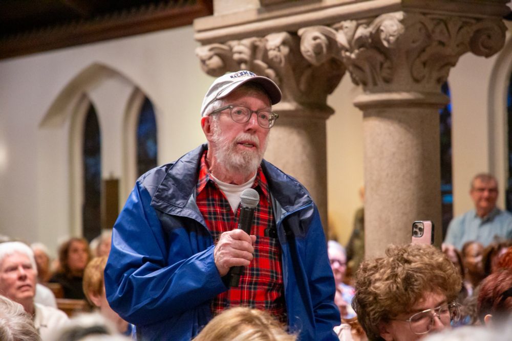 An attendee at the town hall standing up to ask a question, with a microphone in his hand.