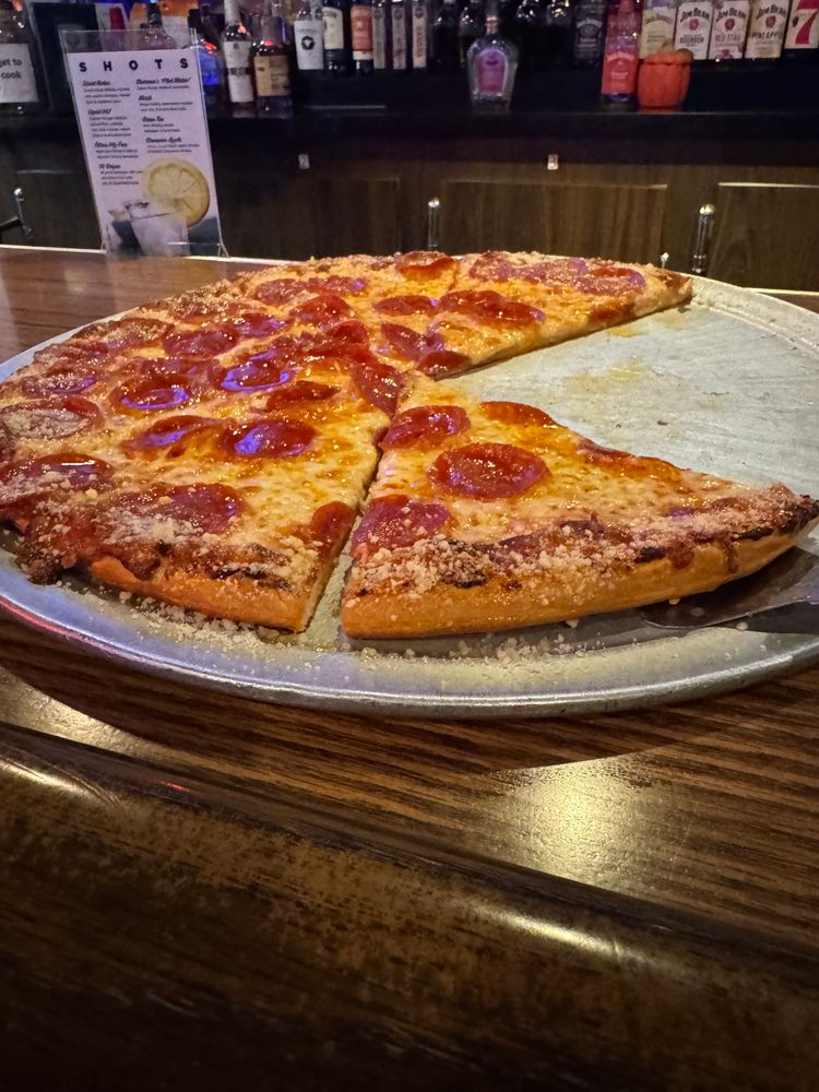 A pepperoni pizza with melted cheese and a dusting of grated Parmesan on the crust, served on a round metal tray with one slice missing.