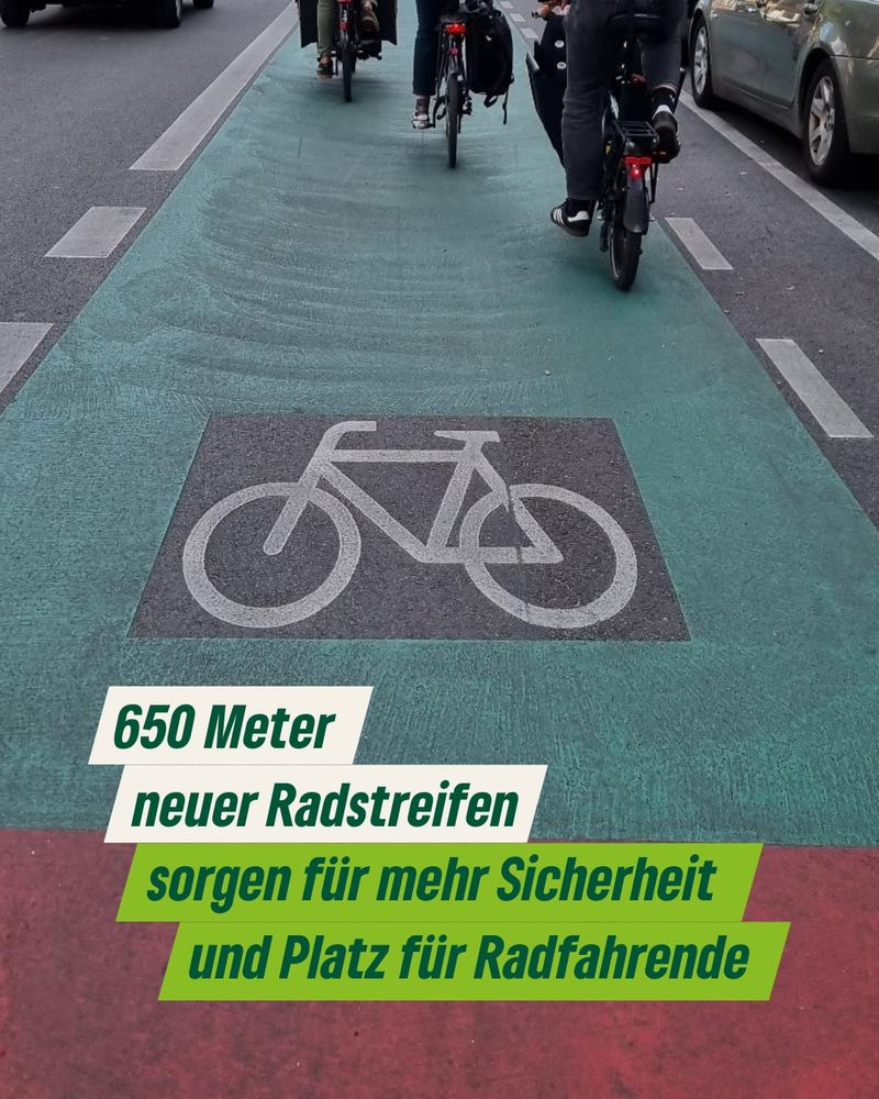 Das Bild zeigt einen großen Fahrradstreifen, der grün und rot markiert wird mit einem Fahrradsymbol darauf. Oben im Bild sieht man drei Fahrräder, die den Fahrradstreifen befahren.