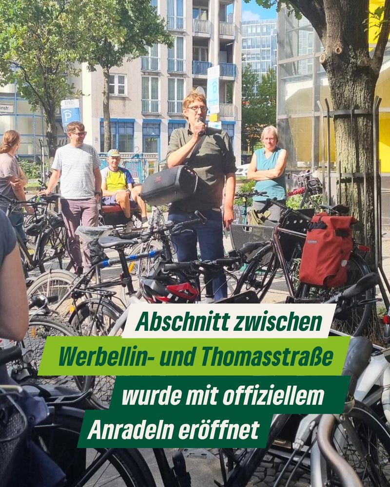Stadtrat Jochen Biedermann spricht in ein Mikrofon an der Kreuzung Hermannstraße/Werbellinstraße. Um ihn herum stehen viele Fahrräder und weitere Personen, die ihm zuhören.