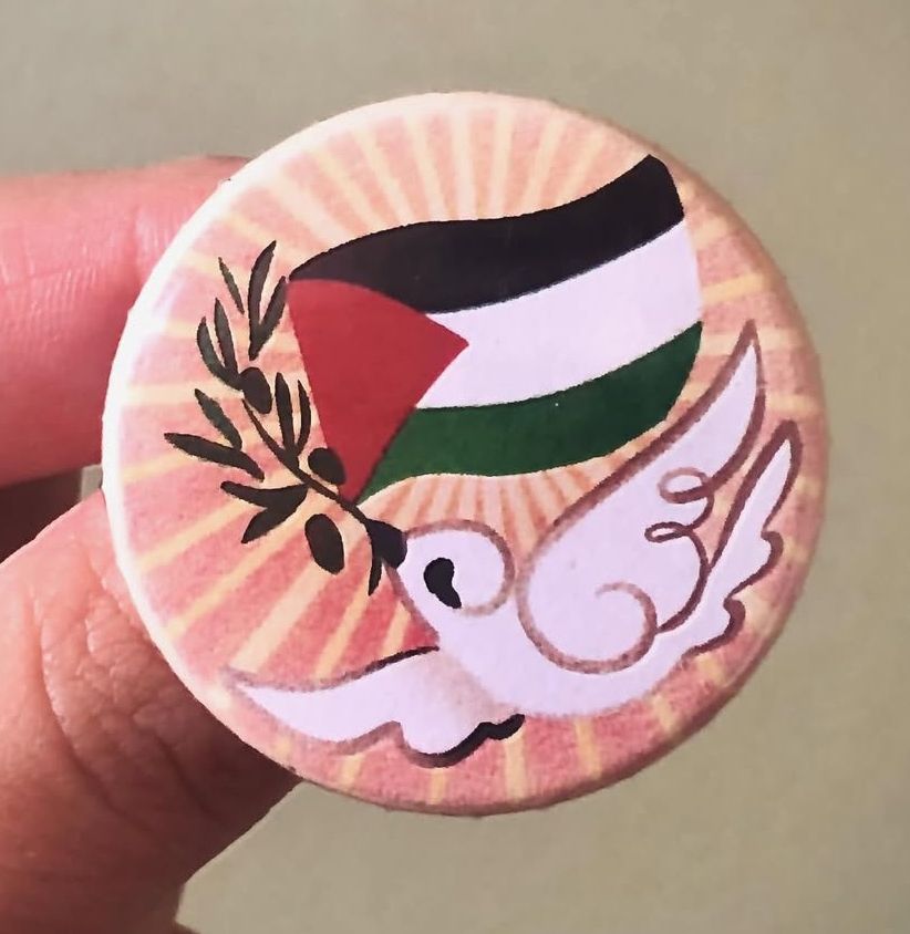 Boton de uma pomba branca segurando um ramo de oliveiras e a bandeira da Palestina. 