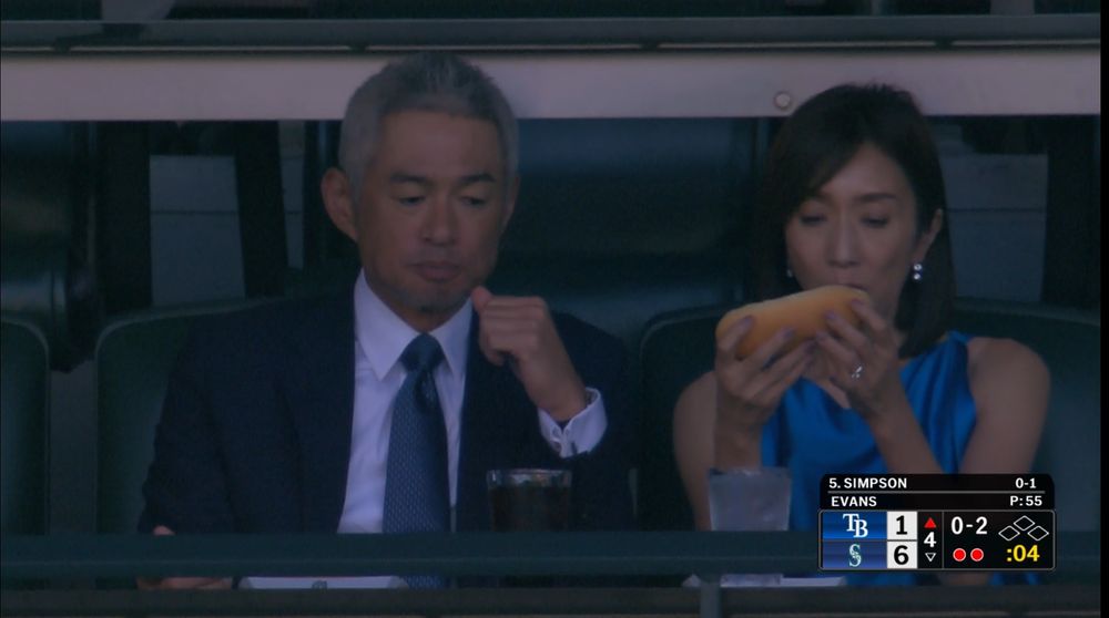 Ichiro and his wife sit in the fancy seats eating hotdogs. 