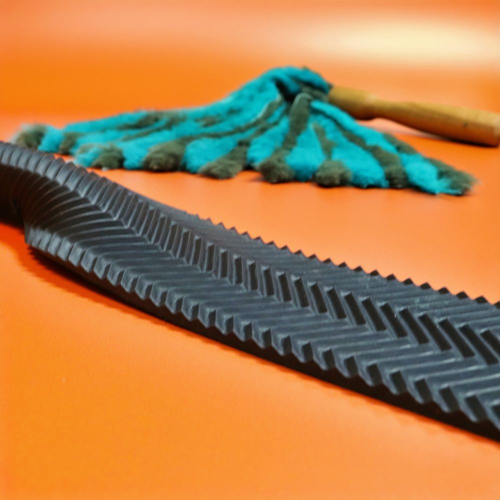 Jade and forest green rabbit fur flogger with wooden handle and ripple rubber double cheek slapper on orange background. Handmade UK BDSM impact toys.
