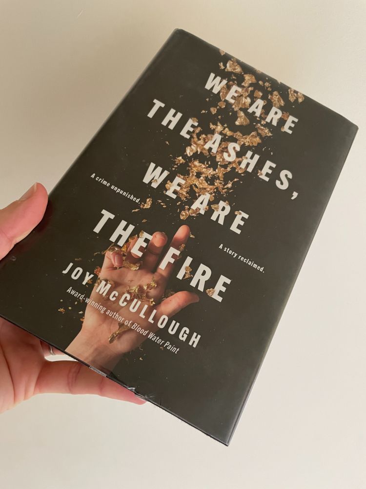 book cover shows a hand at the bottom and golden flakes extending up from the hand; the cover background is black; the title is in white; the photo is the book in my hand with an off-white background