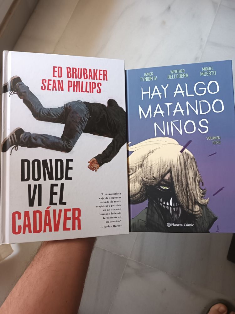 Una mano sujeta dos cómics: "Donde vi el cadáver" y "Hay algo matando niños"