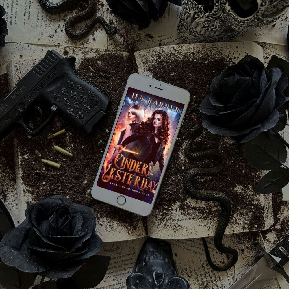 Cinders of Yesterday appears on a phone, surrounded by guns, black roses and snakes. 