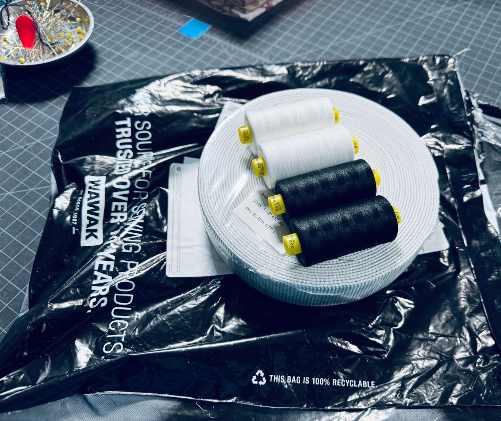 Wawak delivery bag with a roll of elastic, black, and white thread sitting on a sewing table