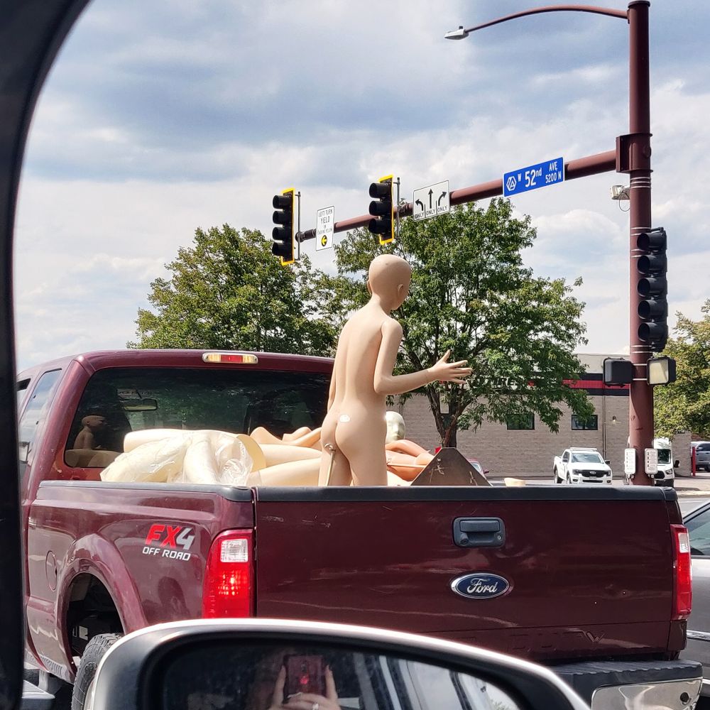 A mannequin stood up in the back of a pickup truck that is driving around. Also that mannequin has a nice ass :)