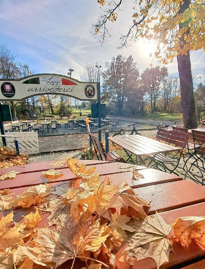 Herbstlaub auf Tisch im Außenbereich einer Gaststätte bei Sonnenschein. Im Hintergrund Schild einer Pizzeria.