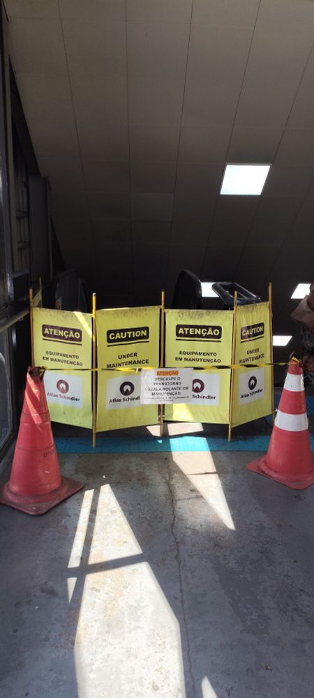 Foto colorida da escada rolante parada, exatamente como a foto anterior, sinalização, plaquinha com erro de português.