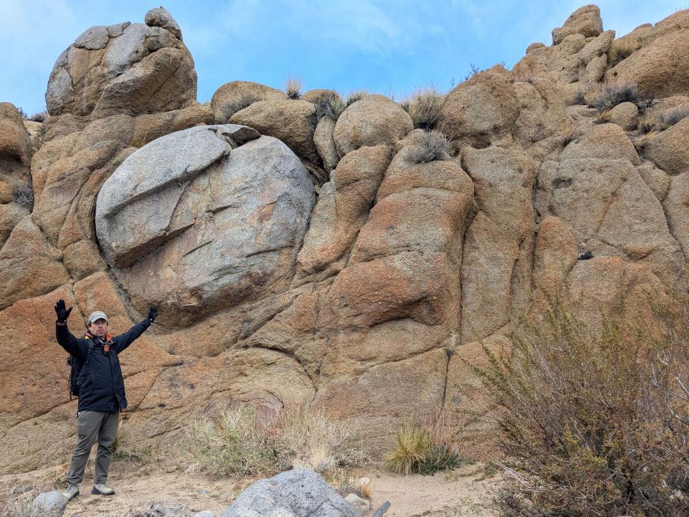 Callan holds his hands above his head in front of an outcrop up jointed and spheroidally weathered granite. A prominent round unweathered portion is just above and to the right of Callan's left hand.