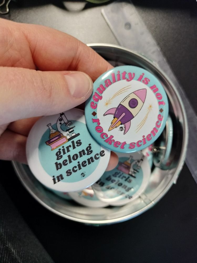 Photo de 2 badges avec écrit :
Girls belong in science
Equality is not rocket science 