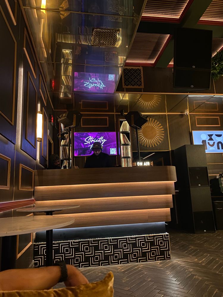 DJ in a corner booth in ambient lighting. Cubes filled with records are behind him.