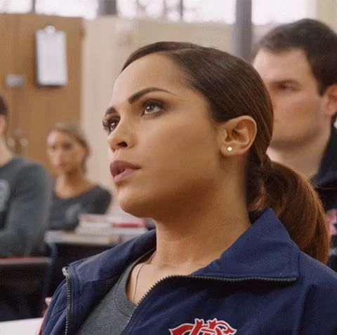 a woman in a blue jacket is sitting in a classroom looking up at the sky .