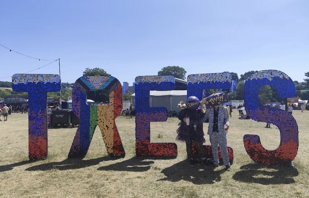 Photo of us dressed as giant miniature heroes in front of an LGBTQ+ themes sign reading "Trees"