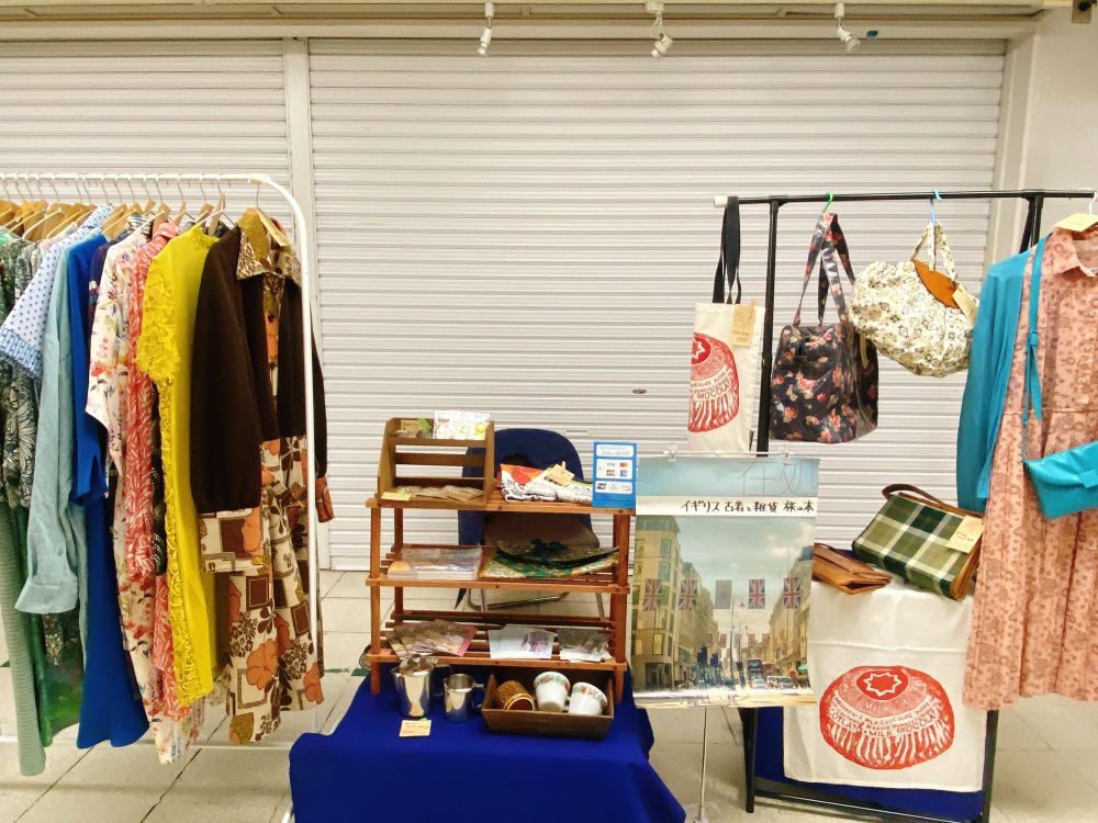 シャッターの閉まった店舗の前の通路に、ハンガーラックや棚が置かれていて、ワンピースやカバン、小物が並べられている