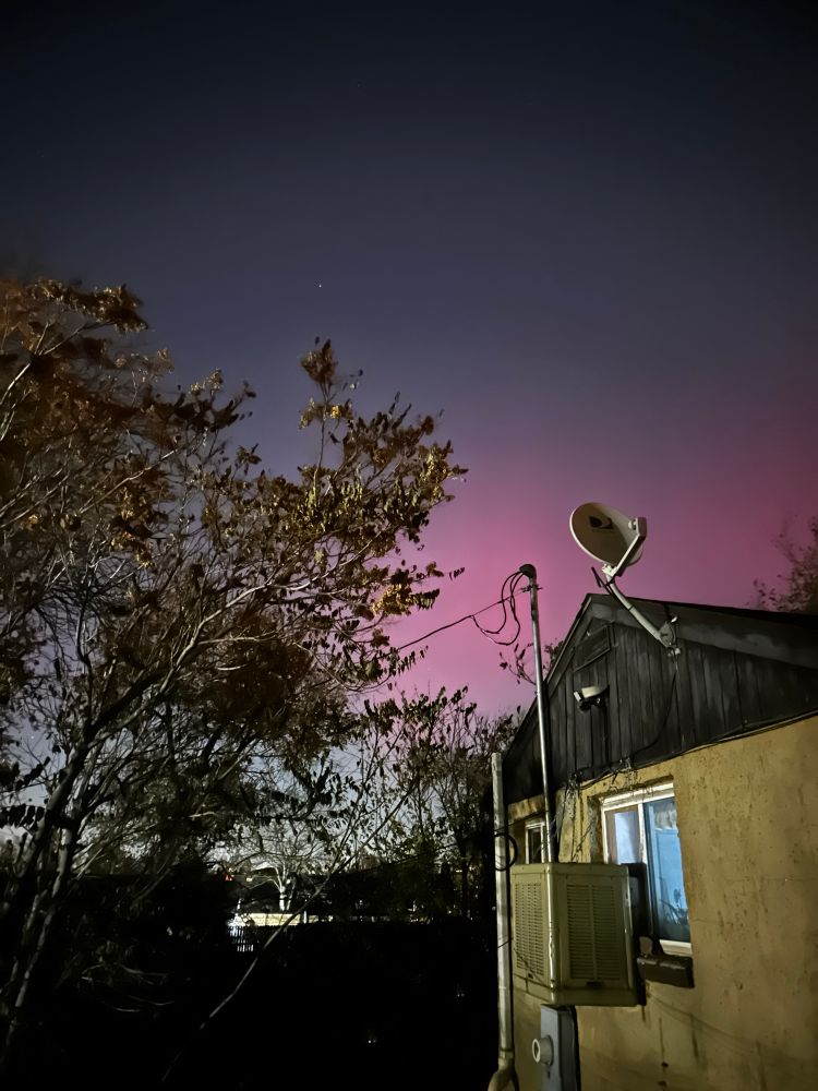 A photo of a house against a night sky which has a pink smudge of northern lights