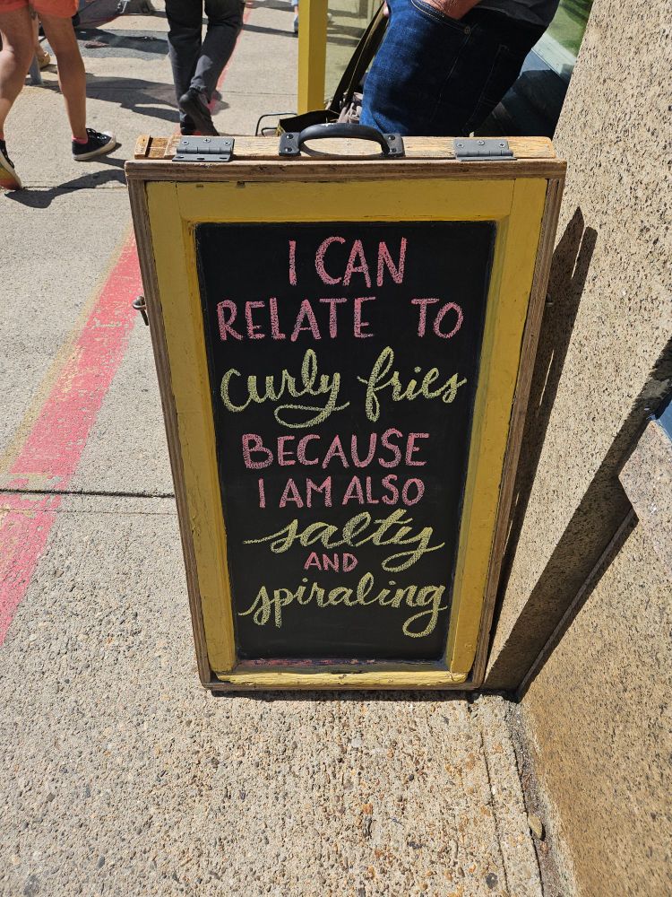 A chalk sign that reads "I can relate to curly fries because I am also salty and spiraling. "