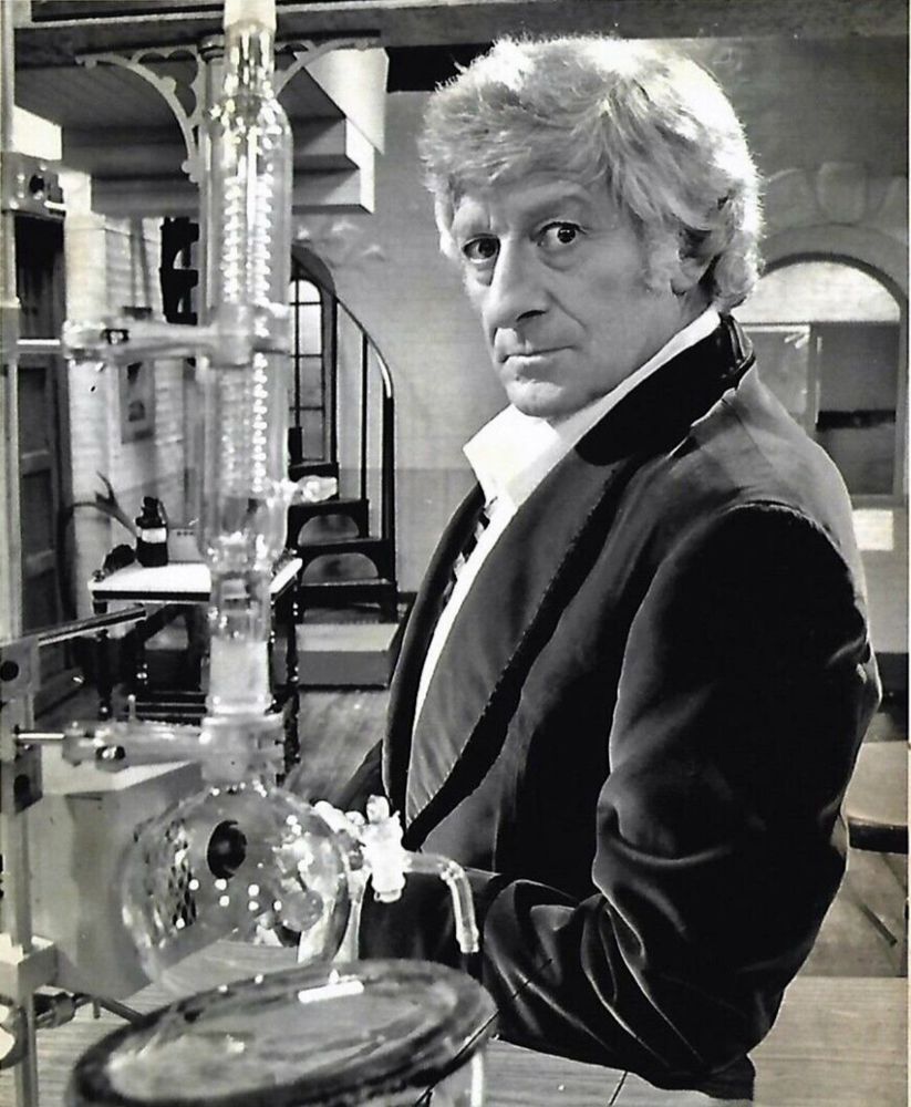 the third doctor played by jon pertwee, in a lab looking towards the camera, black and white image