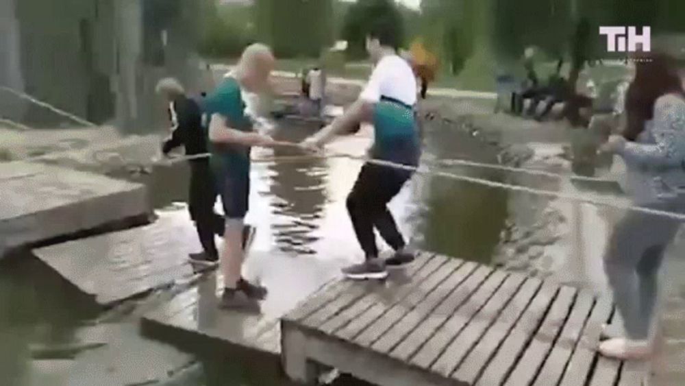 a group of people are standing on a wooden bridge over a river .