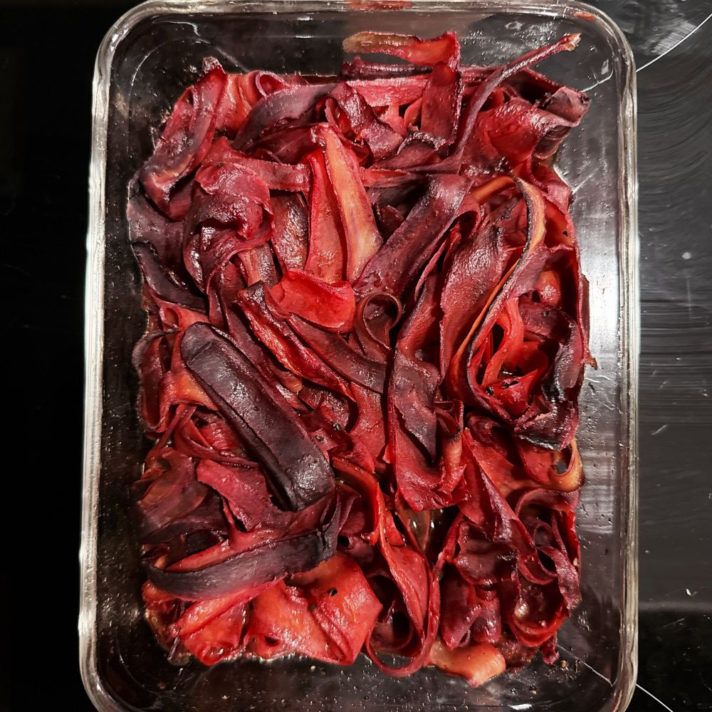 A transparent glass baking dish on top of a black induction cooktop. The dish contains roasted slices of purple carrots.