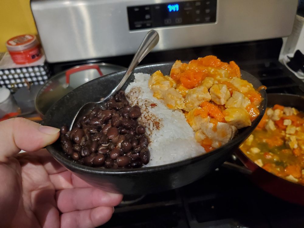 Bowl filled with cooked black beans and pork with vegetables separated by rice in the middle
