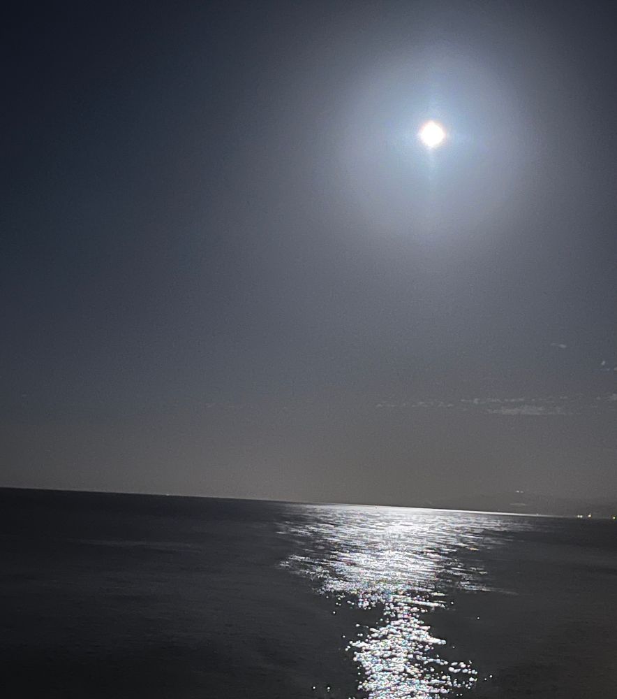 A photo of the full moon hanging over a body of water and reflected therein.