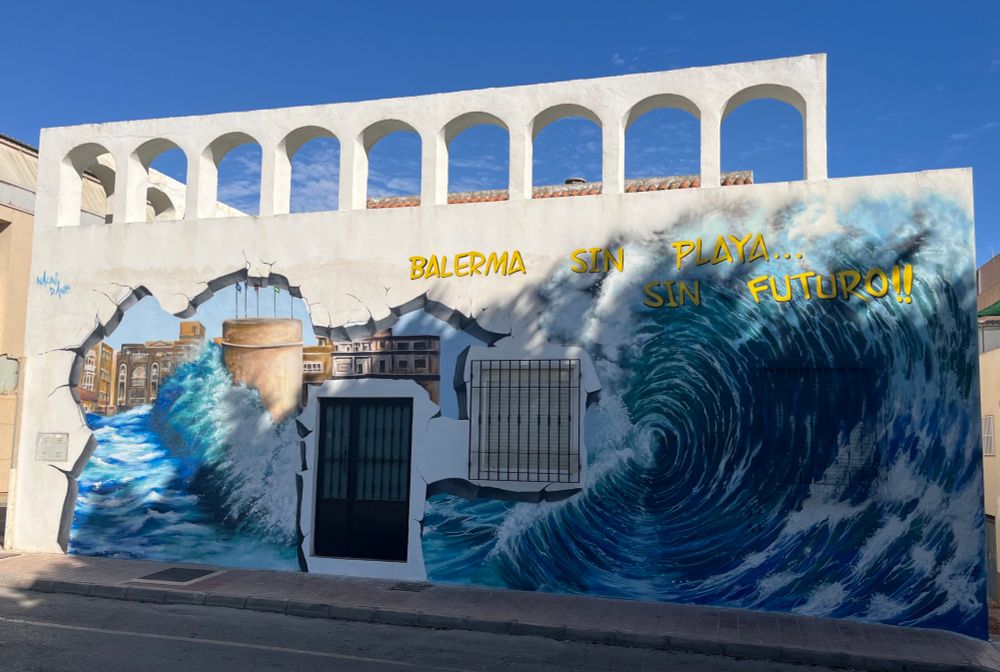 A mural of a violent wave washing over a sea wall. Text: Balerma Sin Playa… Sin Futuro!!! 