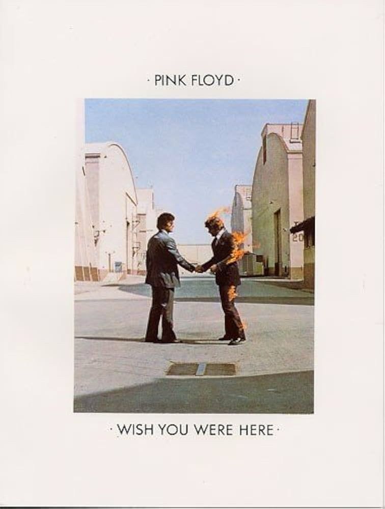 Two men in suits standing in an alley between warehouses. The one of the right is on fire. Pink Floyd Wish You Were Here