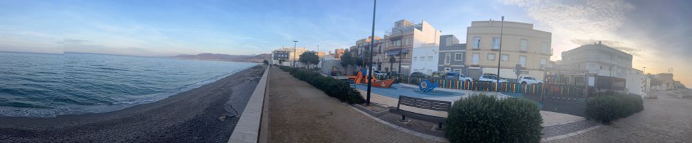 Panoramic photo of the beachfront with apartments and a restaurant to the right. 