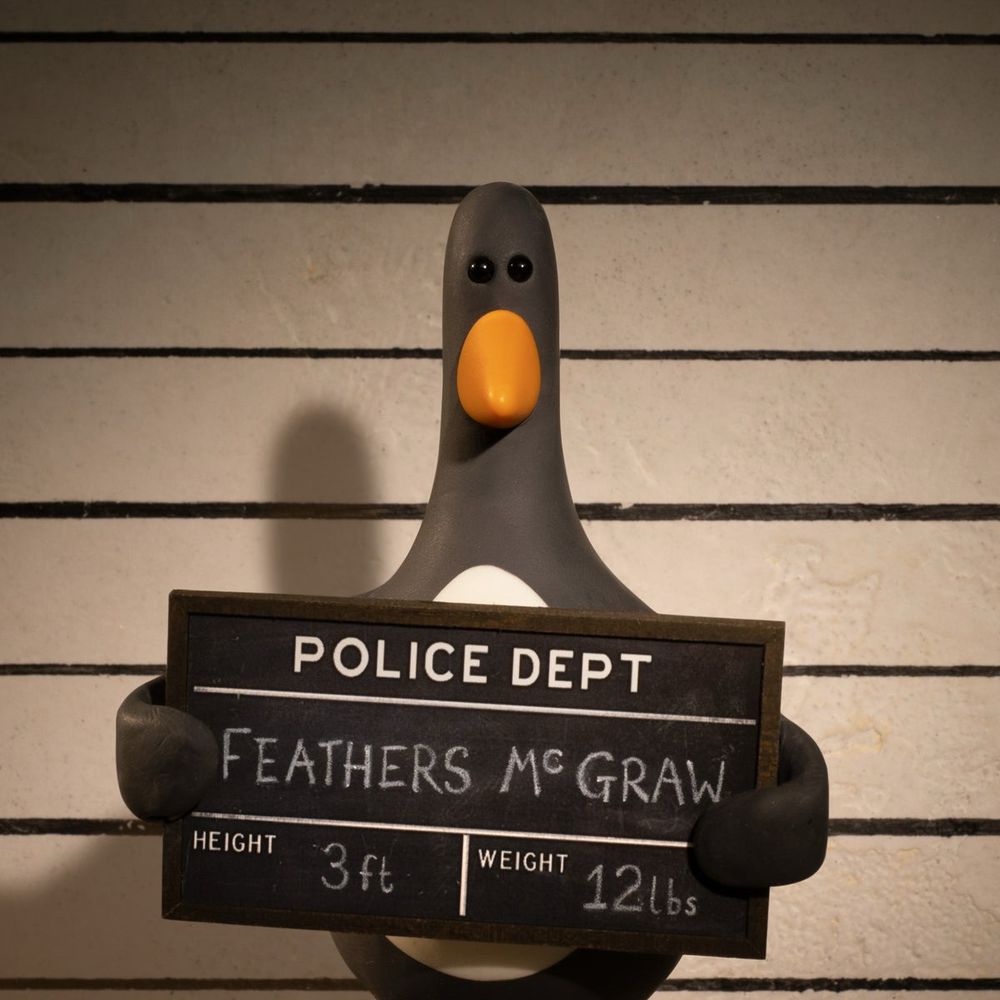 A penguin holds a placard that reads:
Police Department
Feathers McGraw
Height 3 ft Weight 12lbs