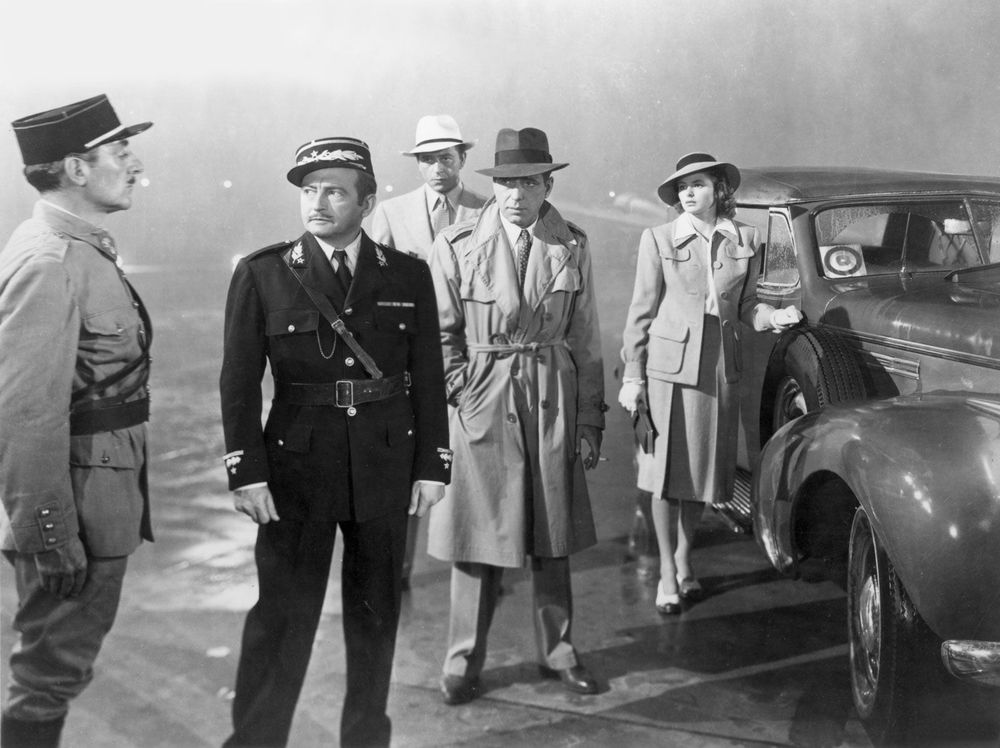 Five people standing next a 1930s automobile in the fog. Three, two men and a woman, are dressed for the weather and looking at the other two, a police captain giving an order to a subordinate.