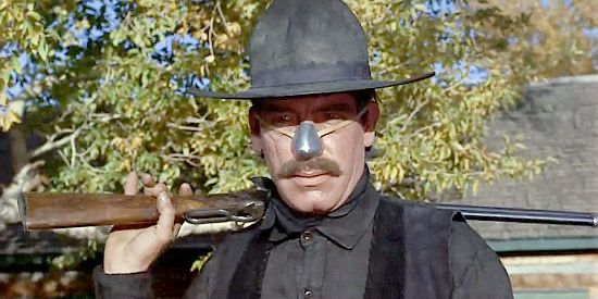 A cowboy dressed in black with a rifle over his shoulder. He is wearing a tin nose.