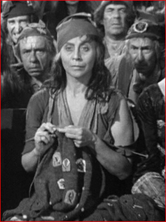 A woman in 18th Century peasant garb knitting and staring at the camera.