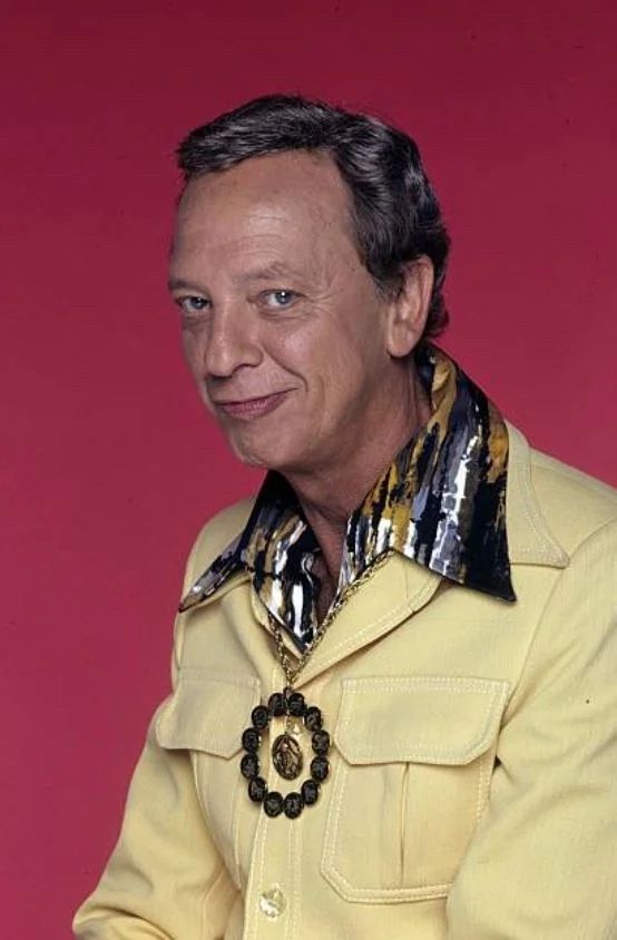 An older man, nicely coiffed, smirking, wearing a very loud yellow jacket.