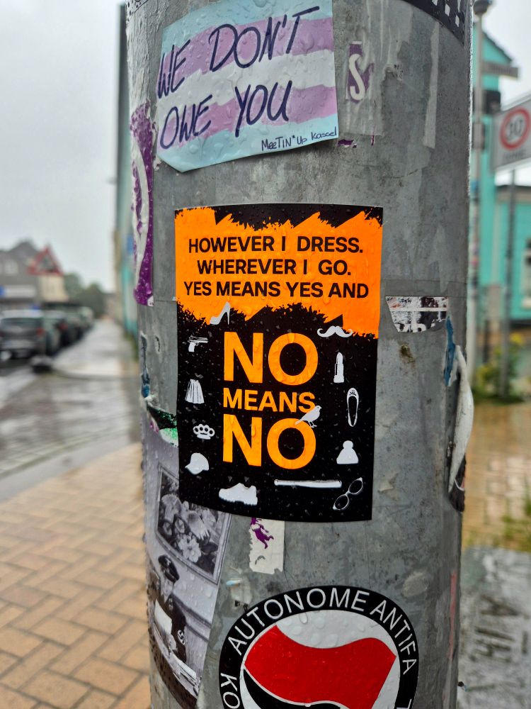 Das Bild zeigt mehrere Sticker an einem Laternenpfahl, darunter ein auffälliger Aufkleber mit der Botschaft: „However I dress. Wherever I go. Yes means yes and NO means NO“ – ein klares Statement gegen sexualisierte Gewalt.