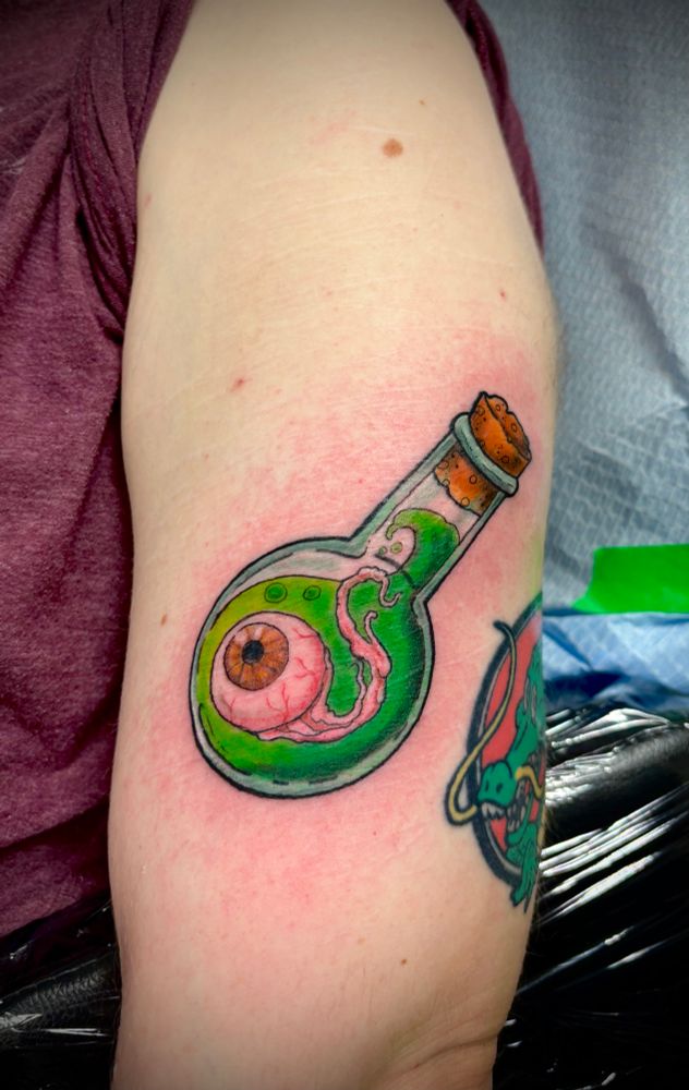 Colourful tattoo of an eyeball floating in bright green liquid in a glass bottle with a cork
