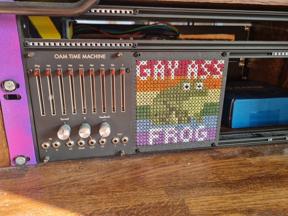 The cross stitch placed on a eurorack synth rail, next to an Olivia Artz Modular Time Machine.