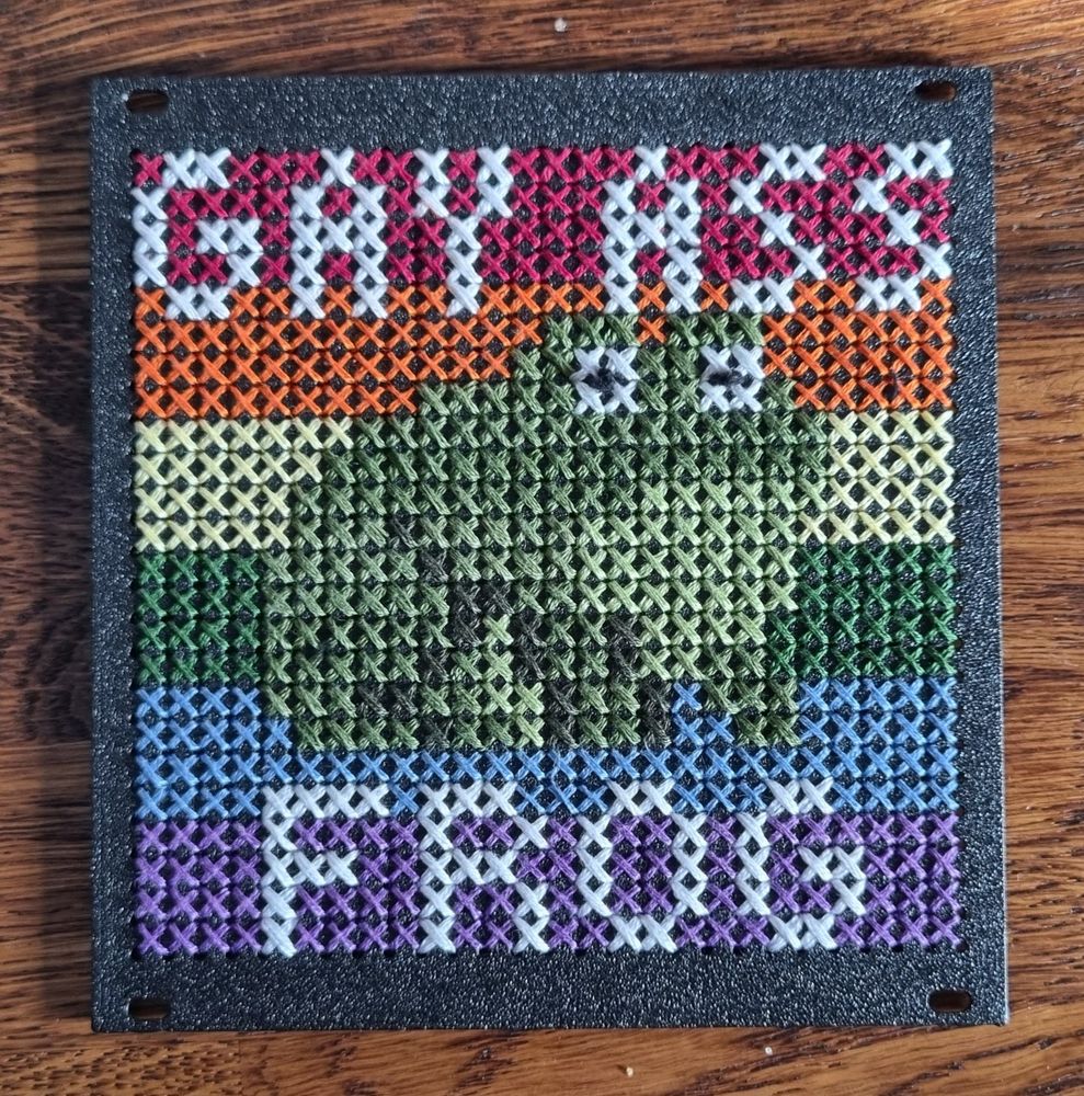 A cross stitch of a frog on a pride flag background. It is captioned "GAY ASS FROG".