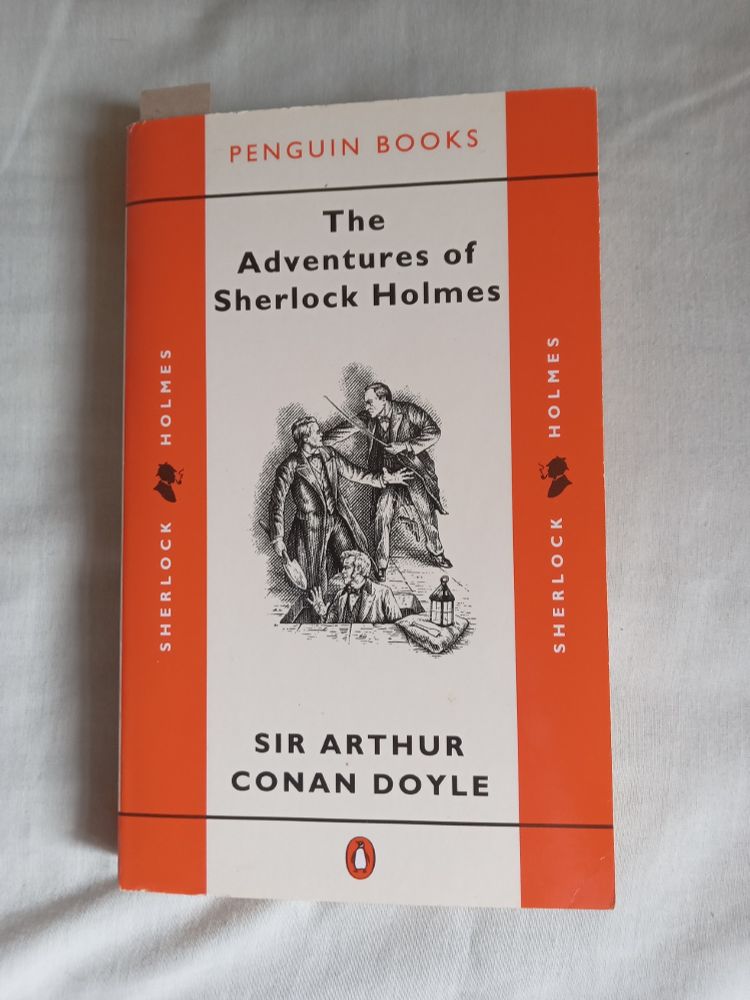 Penguin paperback edition of 'The Adventures of Sherlock Holmes' by Arthur Conan Doyle. In the centre is a b/w drawing of Holmes confronting a man holding a large trowel who has come out of a hole in a paved floor. There is another man emerging from the same hole.