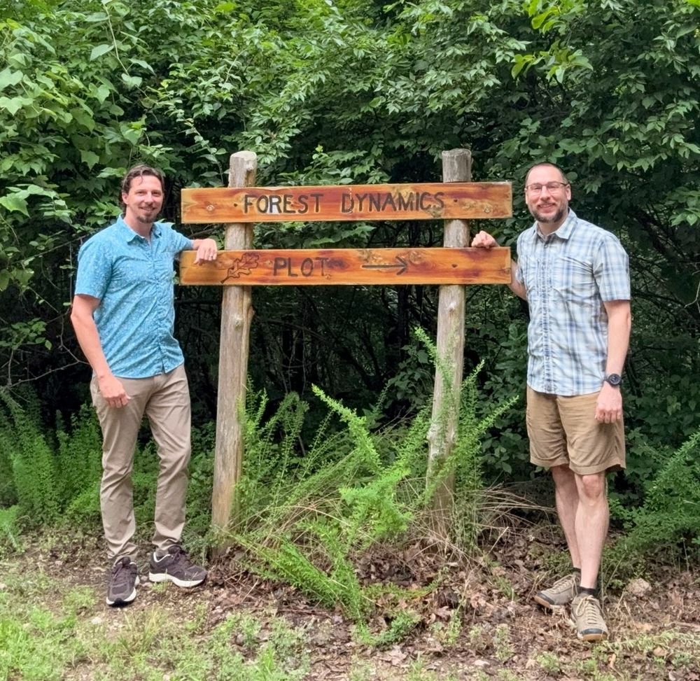 Chris and Jonathan standing in front of a wood sign marking a forest dynamics research site in the foothills of Missouri Ozarks.
