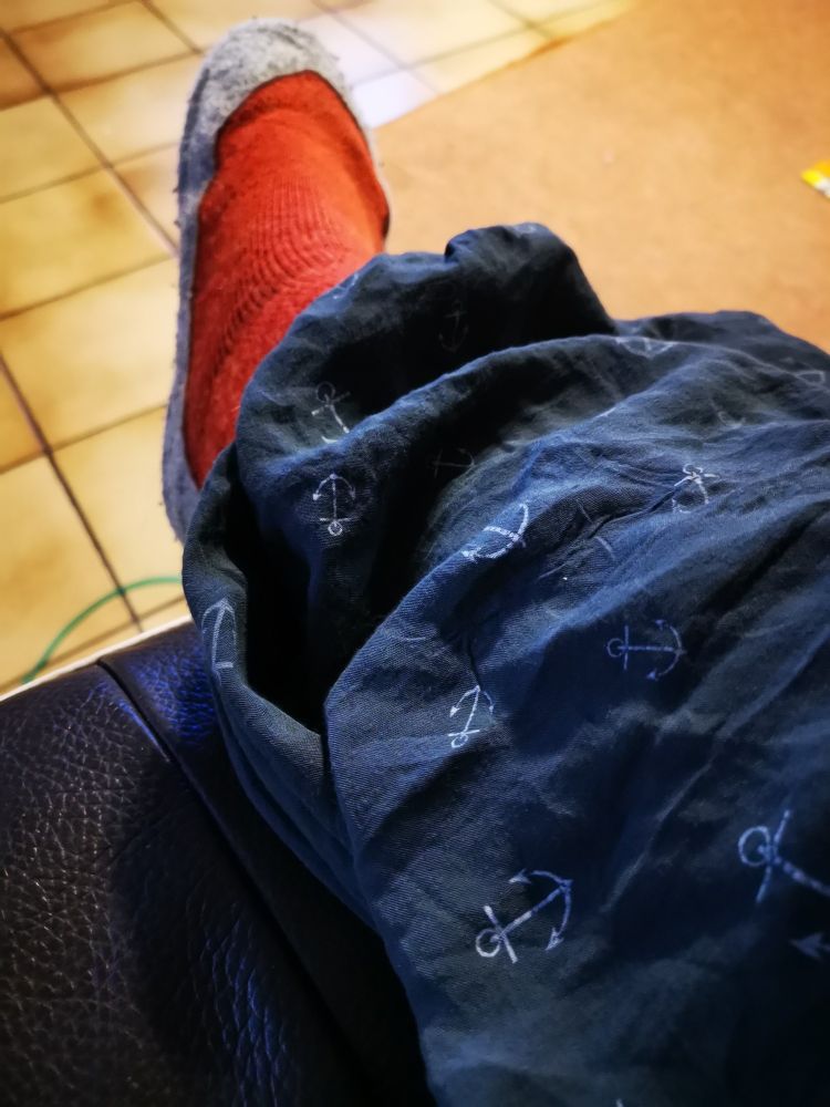 Man sieht ein Bein/Fus in einer weiten Hose und kuscheligen Socken, die auf einer Couch/ Sessel liegt