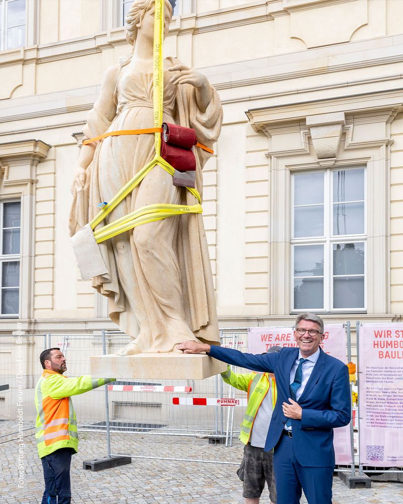 Wolfram Weimer berührt eine der Großfiguren, die gleich mit einem Kran an der Fassade des Humboldt Forums nach oben gezogen wird.