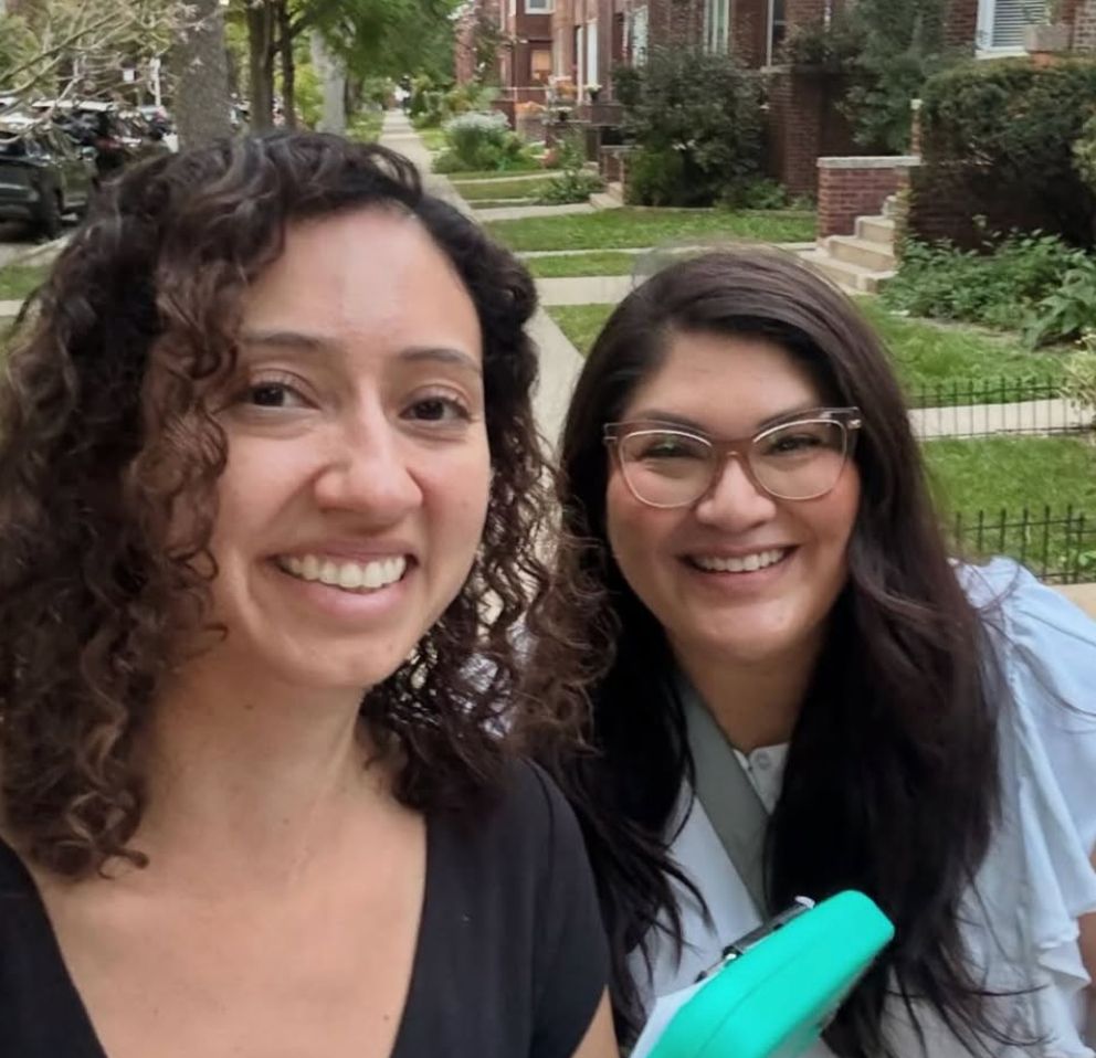 Two people stand outdoors with clipboards smiling. The people are State Senator Graciela Guzman and Cook County Commissioner Jessica Vasquez.