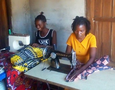Two women sit next to each other sewing fabrics with their refurbished sewing machines.