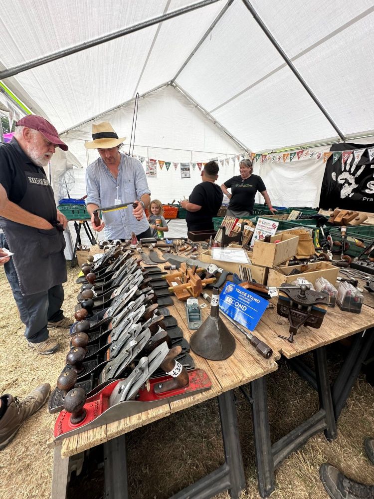 2 People inside the stand looking at tools, and 2 people in the background. There's a table in front of them laid out with tools