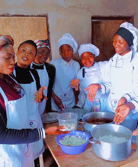 6 women showing what food they have prepared on a table.