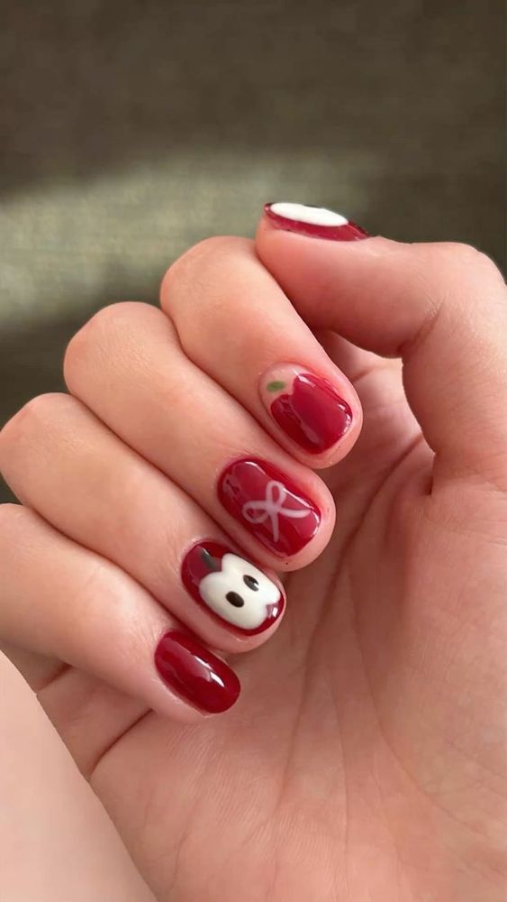 Red nails with half an apple on the ring finger, a pink bow on the middle finger, whole apple on my index finger 