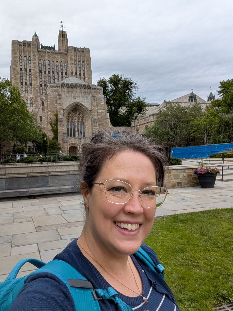 A white woman with glasses and a ponytail stands in front of a library that looks like a castle